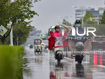 People wear thick clothes and ride in the rain in Qingzhou, China, on October 18, 2024. (