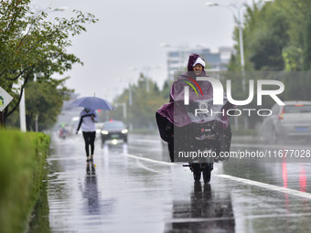 People wear thick clothes and ride in the rain in Qingzhou, China, on October 18, 2024. (