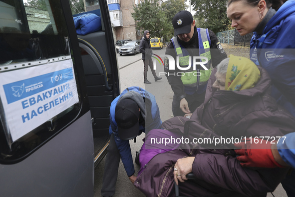 A police officer and volunteers help an elderly woman in a wheelchair get out of the bus at an evacuation point during the arrival of people...