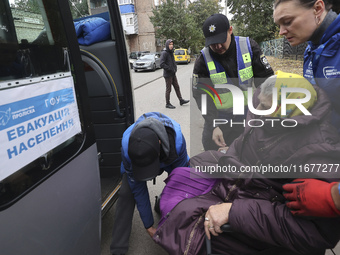 A police officer and volunteers help an elderly woman in a wheelchair get out of the bus at an evacuation point during the arrival of people...