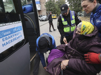 A police officer and volunteers help an elderly woman in a wheelchair get out of the bus at an evacuation point during the arrival of people...