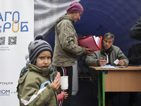 A little boy eats a sandwich as a woman receives help at an evacuation point during the arrival of people from the Kupiansk community in Kha...