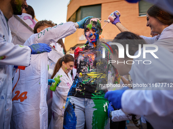 A first-year student from the Faculty of Medicine walks down a hall while seniors paint her with different color paints and glitter as part...