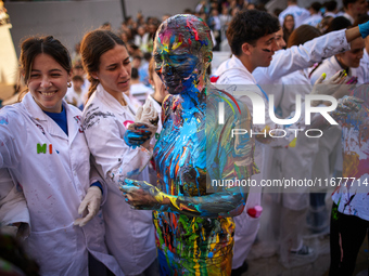 A first-year student from the Faculty of Medicine walks down a hall while seniors paint her with different color paints and glitter as part...