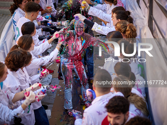 A first-year student from the Faculty of Medicine walks down a hall while seniors paint her with different color paints and glitter as part...