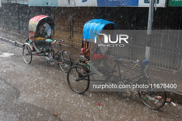 Rickshaw pullers sit under the hood to save themselves from the rain in Dhaka, Bangladesh, on October 18, 2024. 