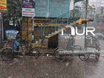 Rickshaw pullers sit under the hood to save themselves from the rain in Dhaka, Bangladesh, on October 18, 2024. (