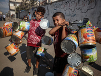 Displaced Palestinian children carry empty cans to sell in the market in Deir al-Balah, Gaza Strip, on October 18, 2024, amid the ongoing wa...