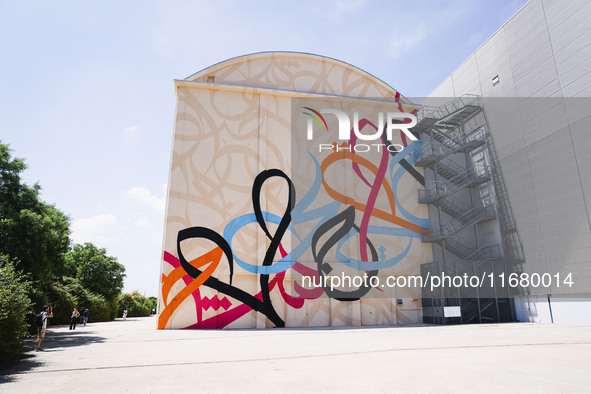 A moment of the press presentation of the mural Waves Only Exist Because the Wind Blows by eL Seed on the exterior walls of Pirelli HangarBi...