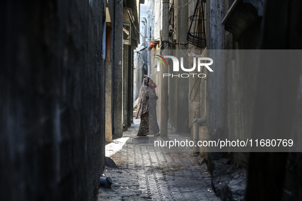 A Palestinian woman carrying a child walks through the Maghazi camp for Palestinian refugees in the central Gaza Strip on October 19, 2024,...