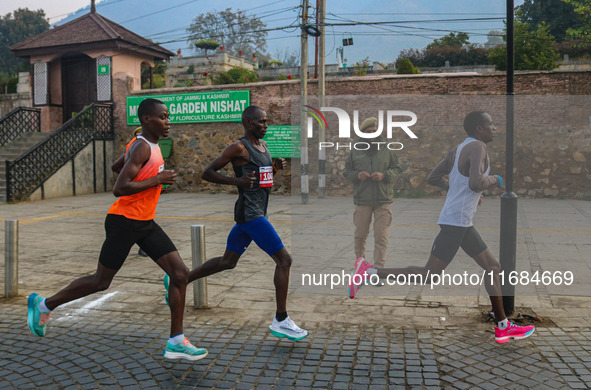 An Indian policeman stands guard as participants run during the Kashmir Marathon on the banks of Dal Lake in Srinagar, Jammu and Kashmir, on...