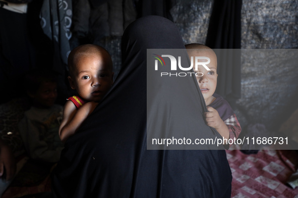 A displaced Palestinian woman carries her children inside her tent in a temporary camp in Khan Yunis, Gaza Strip, on October 20, 2024, amid...