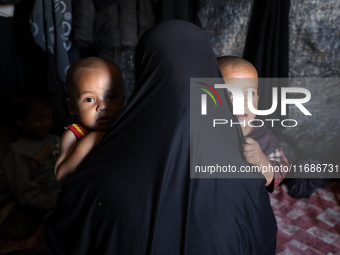 A displaced Palestinian woman carries her children inside her tent in a temporary camp in Khan Yunis, Gaza Strip, on October 20, 2024, amid...