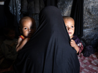 A displaced Palestinian woman carries her children inside her tent in a temporary camp in Khan Yunis, Gaza Strip, on October 20, 2024, amid...