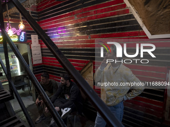 A young Iranian man smokes a cigarette while standing next to his friends at a gaming venue at night in Tabriz, Iran, on October 18, 2024, a...