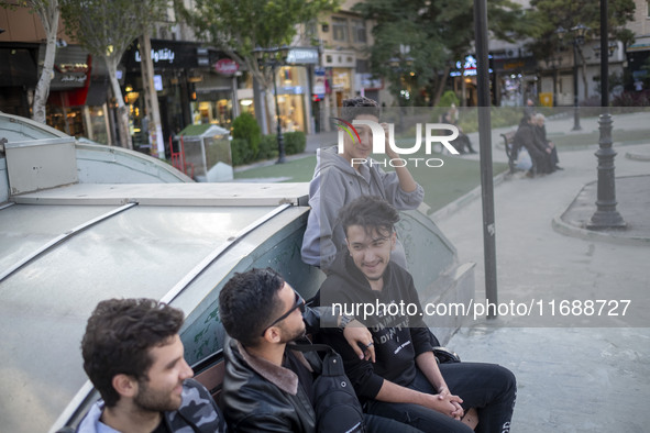 A group of young men sits together on a sidewalk in the historical city of Tabriz, Iran, on October 17, 2024, amid global concerns about war...