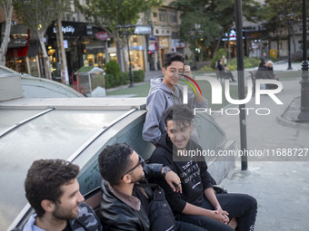 A group of young men sits together on a sidewalk in the historical city of Tabriz, Iran, on October 17, 2024, amid global concerns about war...