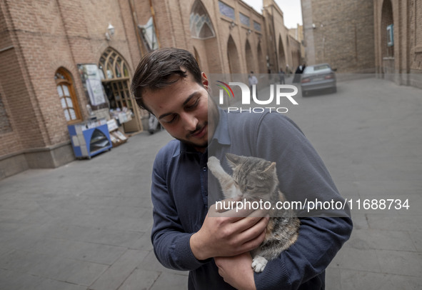 An Iranian man hugs a cat while standing on a street outside the historical mosques in the historical city of Tabriz, Iran, on October 17, 2...