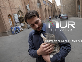 An Iranian man hugs a cat while standing on a street outside the historical mosques in the historical city of Tabriz, Iran, on October 17, 2...