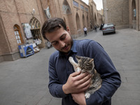 An Iranian man hugs a cat while standing on a street outside the historical mosques in the historical city of Tabriz, Iran, on October 17, 2...