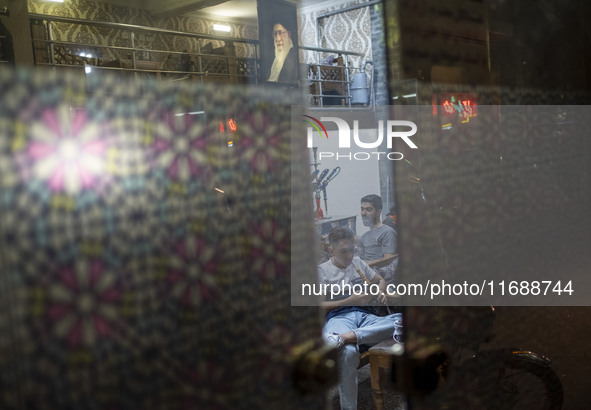 An Iranian man smokes a hookah while sitting under a portrait of Iran's Supreme Leader, Ayatollah Ali Khamenei, at a traditional teahouse at...