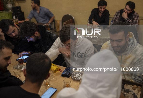 Two young Iranian men trade digital currency on their cellphones while sitting at a cafe at night in Tabriz, Iran, on October 18, 2024, amid...