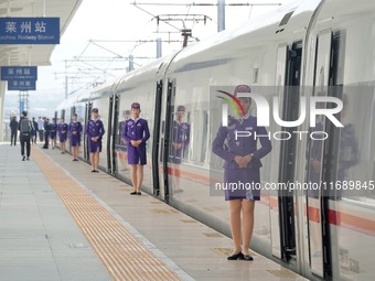 A crew member welcomes passengers to board the first train of the Weifang-Yantai High-Speed Railway at Laizhou Station in Yantai, China, on...