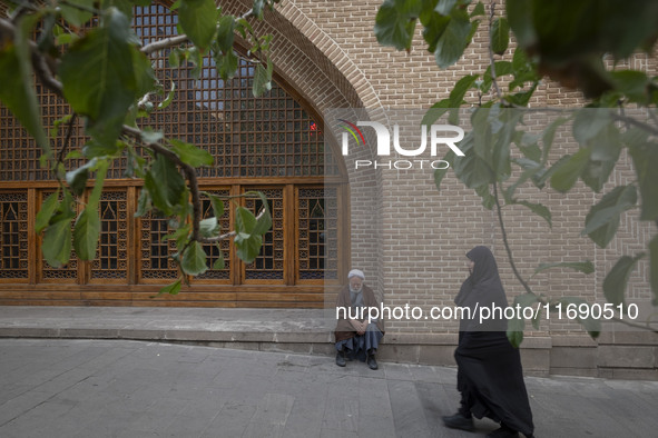 A veiled Iranian woman walks past a cleric sitting in front of a mosque out of a seminary in the historical city of Tabriz, Iran, on October...