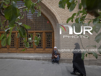 A veiled Iranian woman walks past a cleric sitting in front of a mosque out of a seminary in the historical city of Tabriz, Iran, on October...