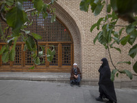 A veiled Iranian woman walks past a cleric sitting in front of a mosque out of a seminary in the historical city of Tabriz, Iran, on October...