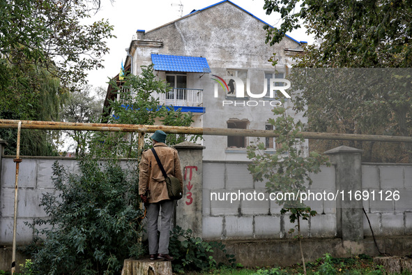 A man stands on a stump and looks at a sanatorium damaged by the October 18 Russian missile strike from behind a brick fence in Odesa, Ukrai...