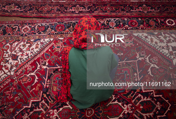 A young Iranian woman sits on a Persian handwoven carpet at a historical mosque in the historical city of Tabriz, located 624 km (388 miles)...