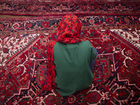 A young Iranian woman sits on a Persian handwoven carpet at a historical mosque in the historical city of Tabriz, located 624 km (388 miles)...