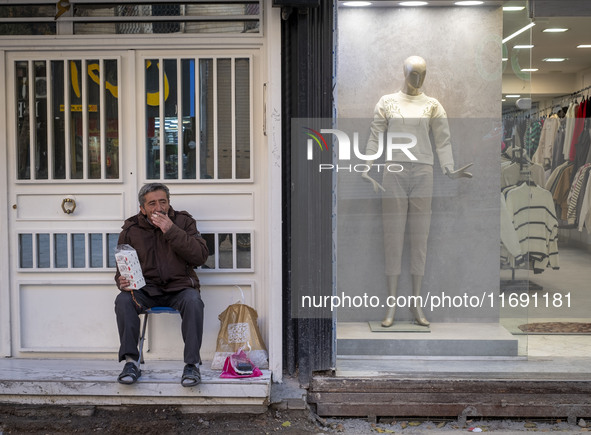 An Iranian vendor smokes a cigarette while sitting next to a mannequin decorated at a shop window in the historical city of Tabriz, Iran, on...