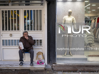 An Iranian vendor smokes a cigarette while sitting next to a mannequin decorated at a shop window in the historical city of Tabriz, Iran, on...