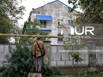 A man stands on a stump and looks at a sanatorium damaged by the October 18 Russian missile strike from behind a brick fence in Odesa, Ukrai...