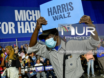 An attendee dances to music while holding a Harris-Walz sign before former President Barack Obama speaks at a presidential campaign rally fo...