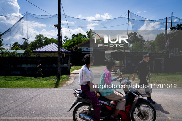 People on a motorcycle pass by an army base in Pattani. Special Forces, the Black Army, and Volunteer Force Operations in Thailand's Deep So...