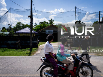 People on a motorcycle pass by an army base in Pattani. Special Forces, the Black Army, and Volunteer Force Operations in Thailand's Deep So...