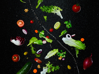 Creative food photography: Fresh salad ingredients suspend in mid-air against a dark background. The composition features lettuce leaves, ch...