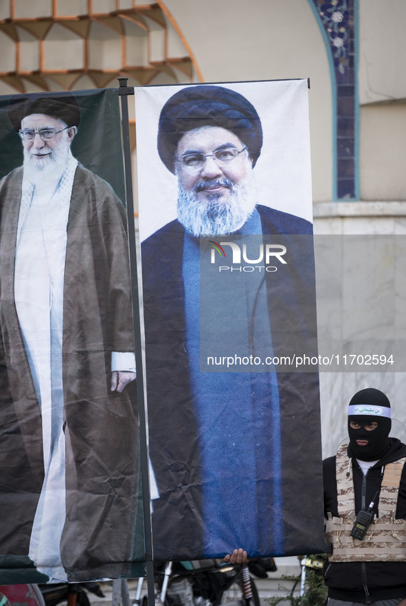 An Islamic Revolutionary Guard Corps (IRGC) personnel, wearing a mask and a uniform symbolizing a Hamas warrior, stands next to the portrait...