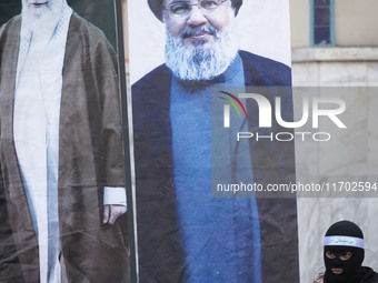 An Islamic Revolutionary Guard Corps (IRGC) personnel, wearing a mask and a uniform symbolizing a Hamas warrior, stands next to the portrait...