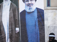 An Islamic Revolutionary Guard Corps (IRGC) personnel, wearing a mask and a uniform symbolizing a Hamas warrior, stands next to the portrait...