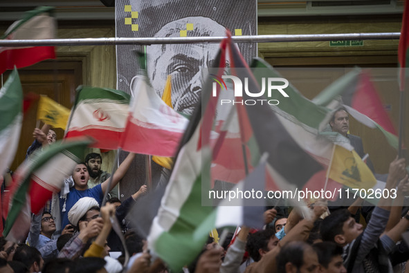 Iranian people wave Palestinian and Iranian flags in front of a banner featuring a portrait of the killed Hamas Leader, Yahya Sinwar, during...