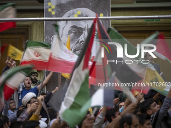 Iranian people wave Palestinian and Iranian flags in front of a banner featuring a portrait of the killed Hamas Leader, Yahya Sinwar, during...