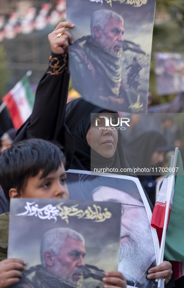 An Iranian schoolboy and a woman hold portraits of the killed Hamas Leader, Yahya Sinwar, while they take part in a ceremony commemorating S...