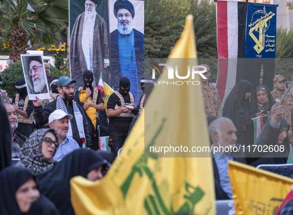 Islamic Revolutionary Guard Corps (IRGC) personnel, wearing masks and uniforms symbolizing Hamas warriors, stand under portraits of Iran's S...