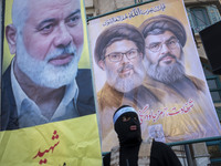 An Islamic Revolutionary Guard Corps (IRGC) personnel, wearing a mask and a uniform symbolizing a Hamas warrior, stands under portraits of L...