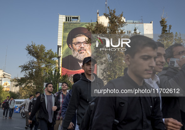 Young Iranian men walk under a giant banner featuring a portrait of Lebanon's Hezbollah Secretary General, Hashem Safieddine, who is killed...