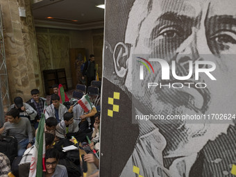 Young men hold Iranian flags and sit next to a banner featuring a portrait of the killed Hamas Leader, Yahya Sinwar, while taking part in a...